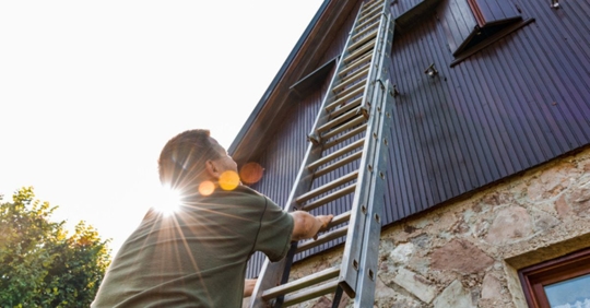 man moving ladder on side of home
